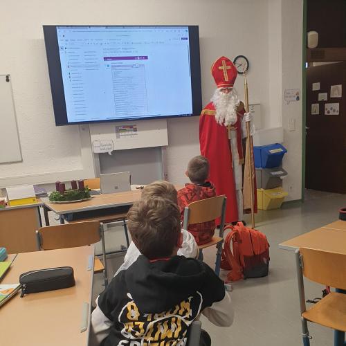 Nikolaus besucht eine Klasse an der MS Kematen und steht neben dem Activeboard und spricht zu den Schüler:innen
