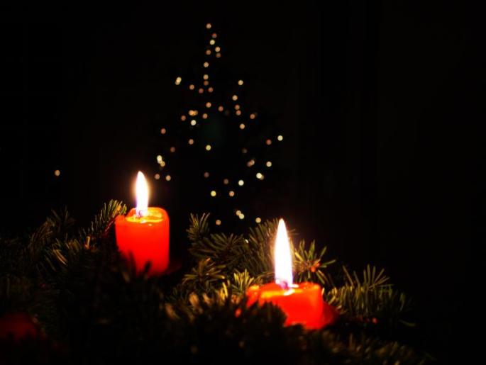 zwei brennende rote Kerzen auf Fichtenzweige im schwarzen Hintergrund funkelnde Lichter in Form eines Baumes