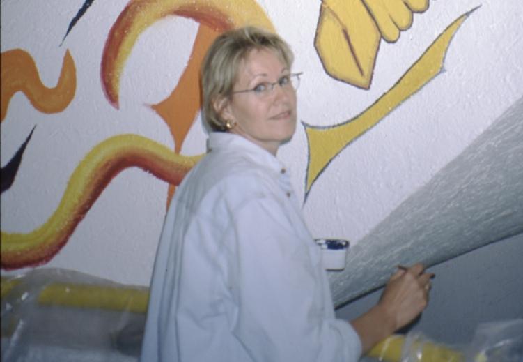 Siess Christine beim Malen einer Stiegenwange. Ornamente und Schriftzug in orange und gelb